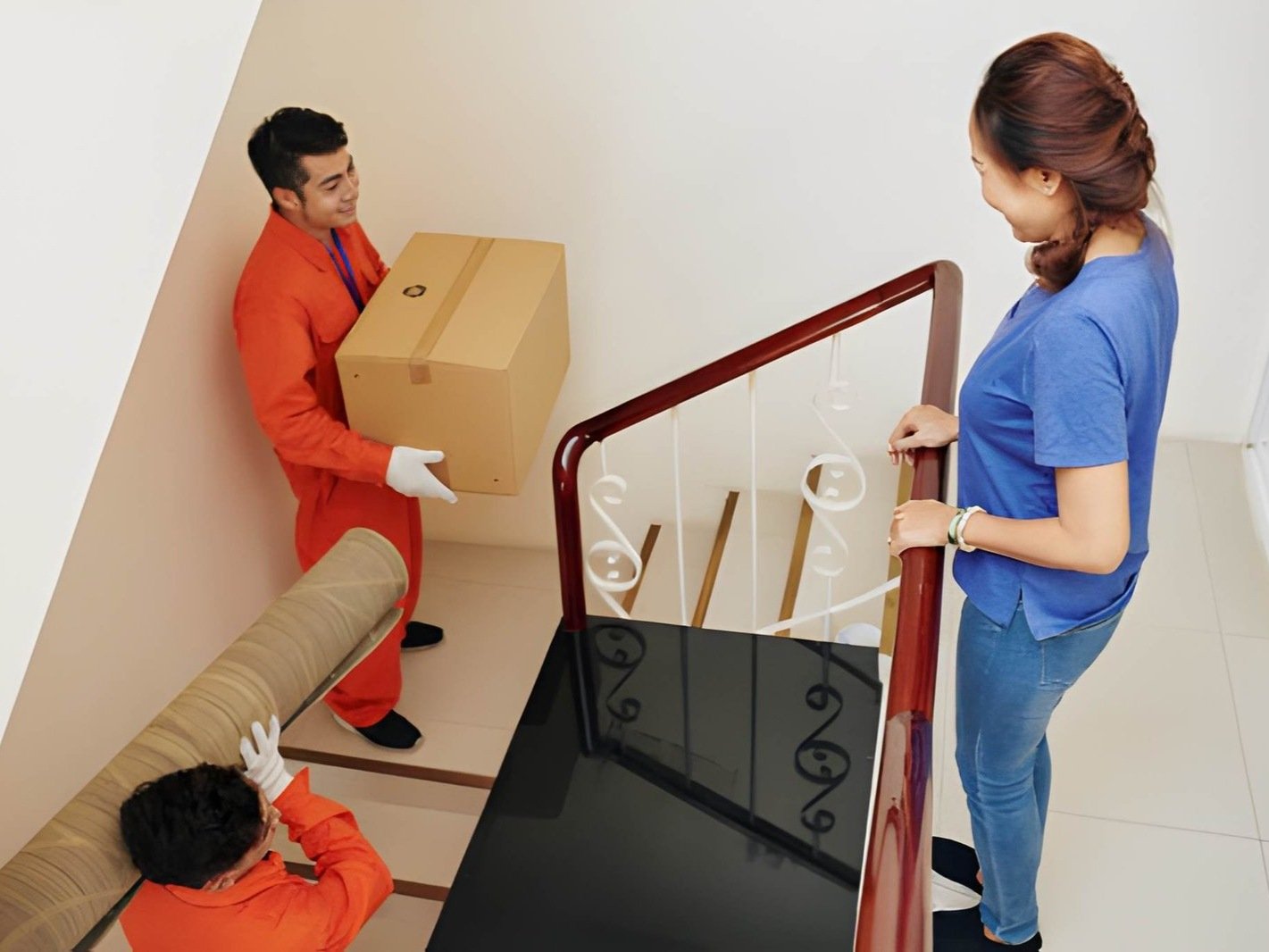 Two movers are carrying a large cardboard box up